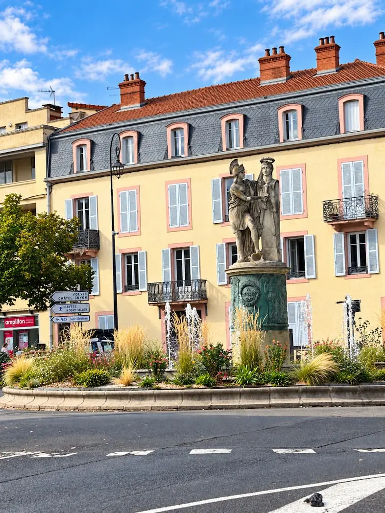 Fontaine ornée de statues devant des façades aux volets clairs à Riom